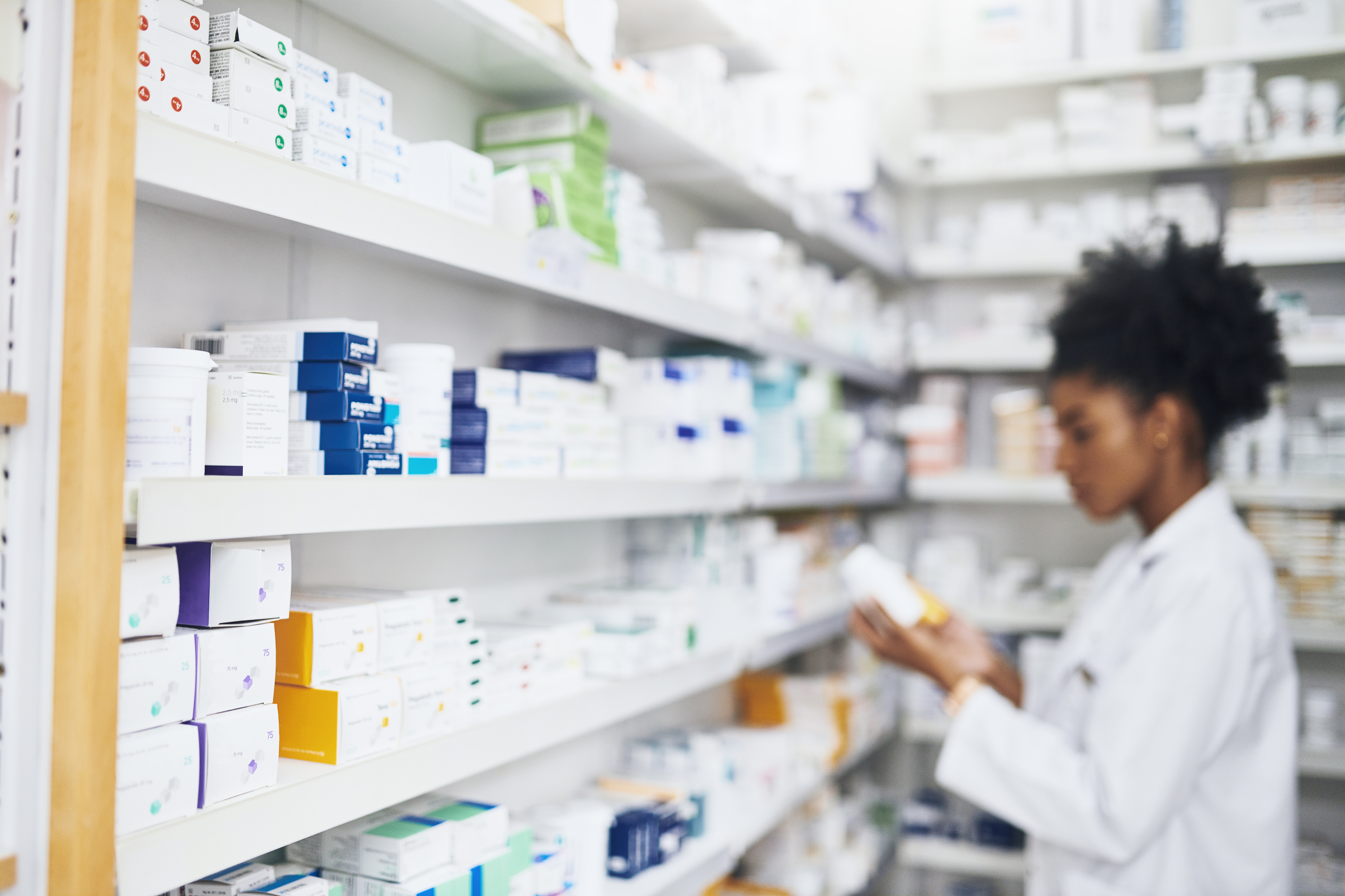 Pharmacy, healthcare and woman with box to check medical info, shelf inventory or price. Prescription medicine, stock and pharmacist reading product label for health benefits of pharmaceutical drugs.