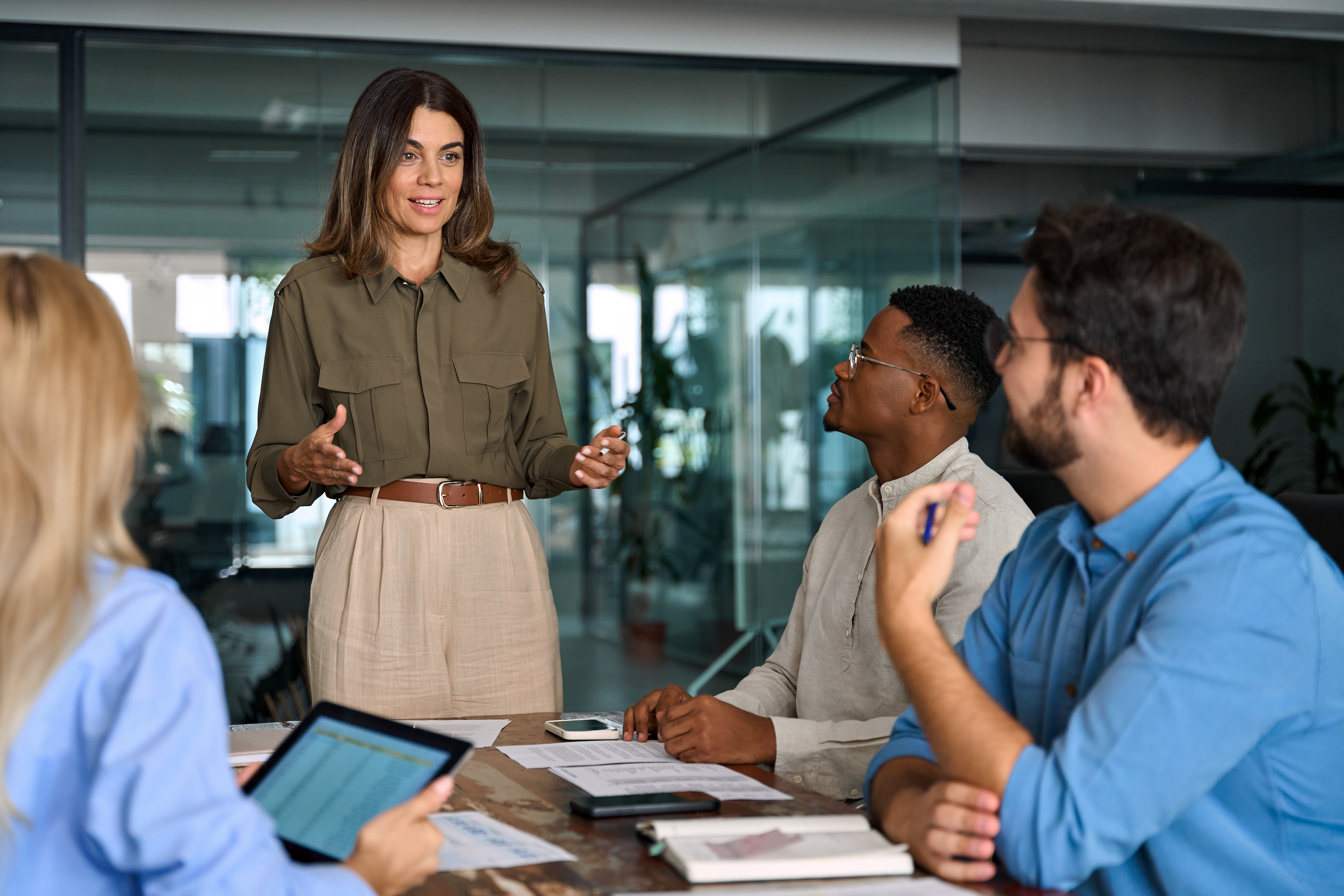 Group of employees sitting around table, woman standing talking