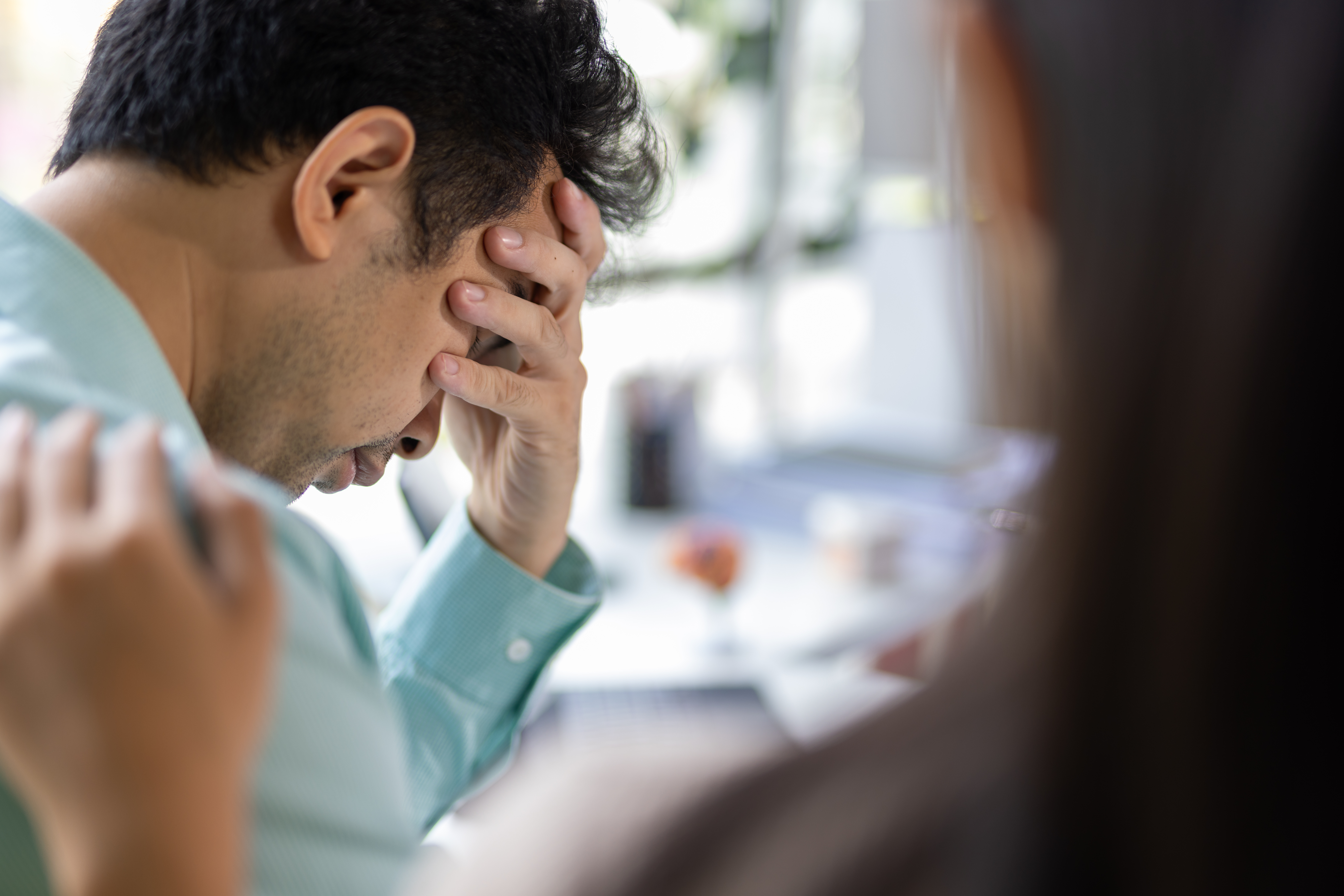 A grieving male patient covering his face while his wife comforts and encourages him at the clinic.