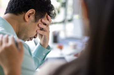 A grieving male patient covering his face while his wife comforts and encourages him at the clinic.