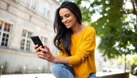 Woman looking at phone, sitting outside, smiling