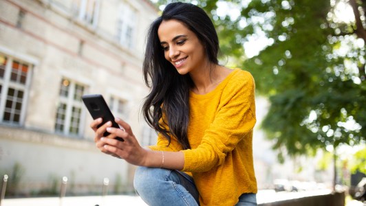 Woman looking at phone, sitting outside, smiling