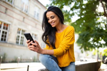Woman looking at phone, sitting outside, smiling