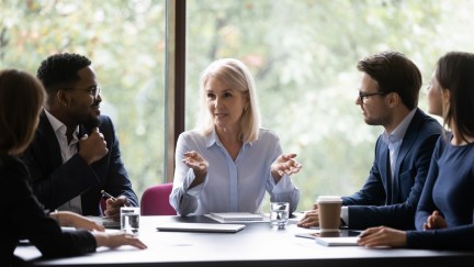 Woman sitting at head of conference table in office, leading group, talking