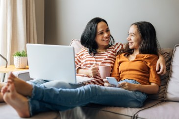 Mom and daughter sitting on couch talking, smiling