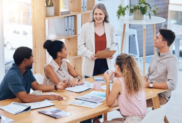 Woman standing, speaking to seated, listening employees