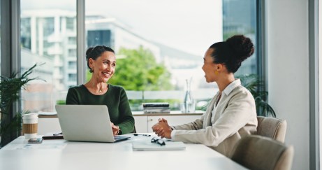 Manager speaking with employee, sitting at table, smiling, in office