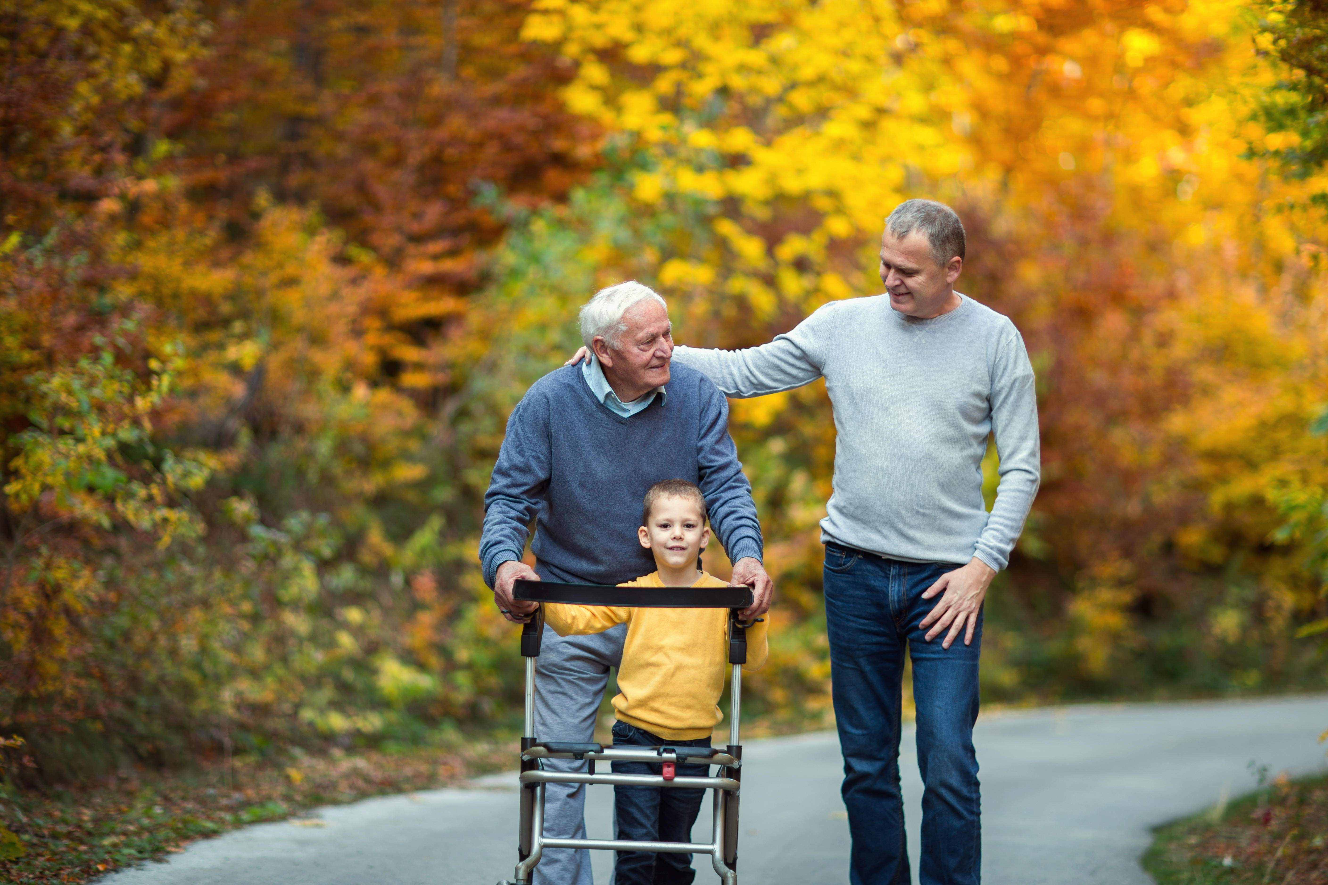 Three generations walking outside together, older man with walker, son and grandson