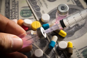 Man's fingers holding small bottle of medicine with syringe; medication; money