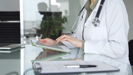 Doctor woman accessing patient data on digital tablet, managing healthcare records in modern medical office. Medicine, health care and science concept.