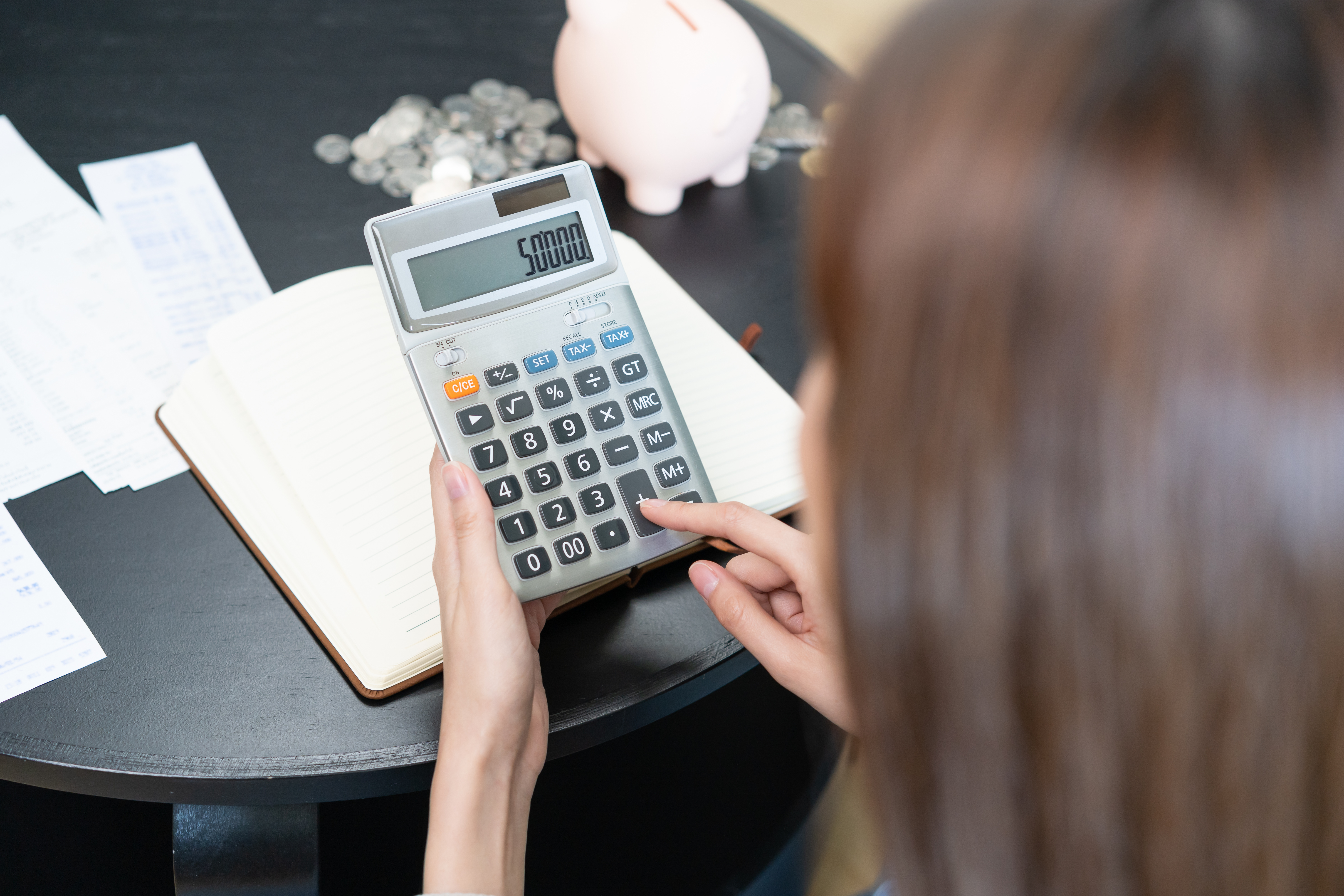 Woman typing on calculator, money and piggy bank on table