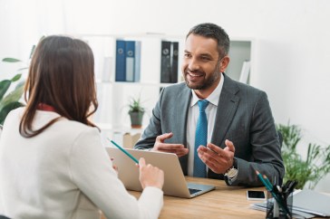 selective focus of advisor sitting at table with laptop and woman in office.