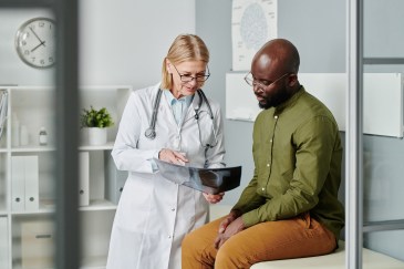 Young adult man wearing glasses and green shirt speaking with female doctor