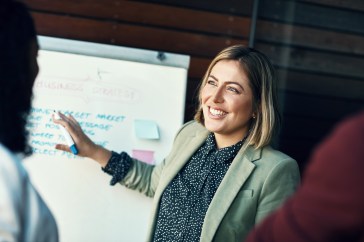 Presentation whiteboard, audience and happy woman planning, coaching and present strategy, ideas or office plan. Sales workshop, project management and team leader, boss or person speaking to group