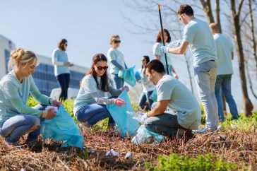 Volunteers with garbage bags cleaning park area.