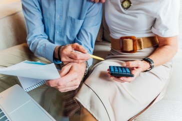 Elderly couple managing household finances and retirement planning, calculating expenses and reviewing bills on a laptop, stressing budget and financial consulting for seniors.