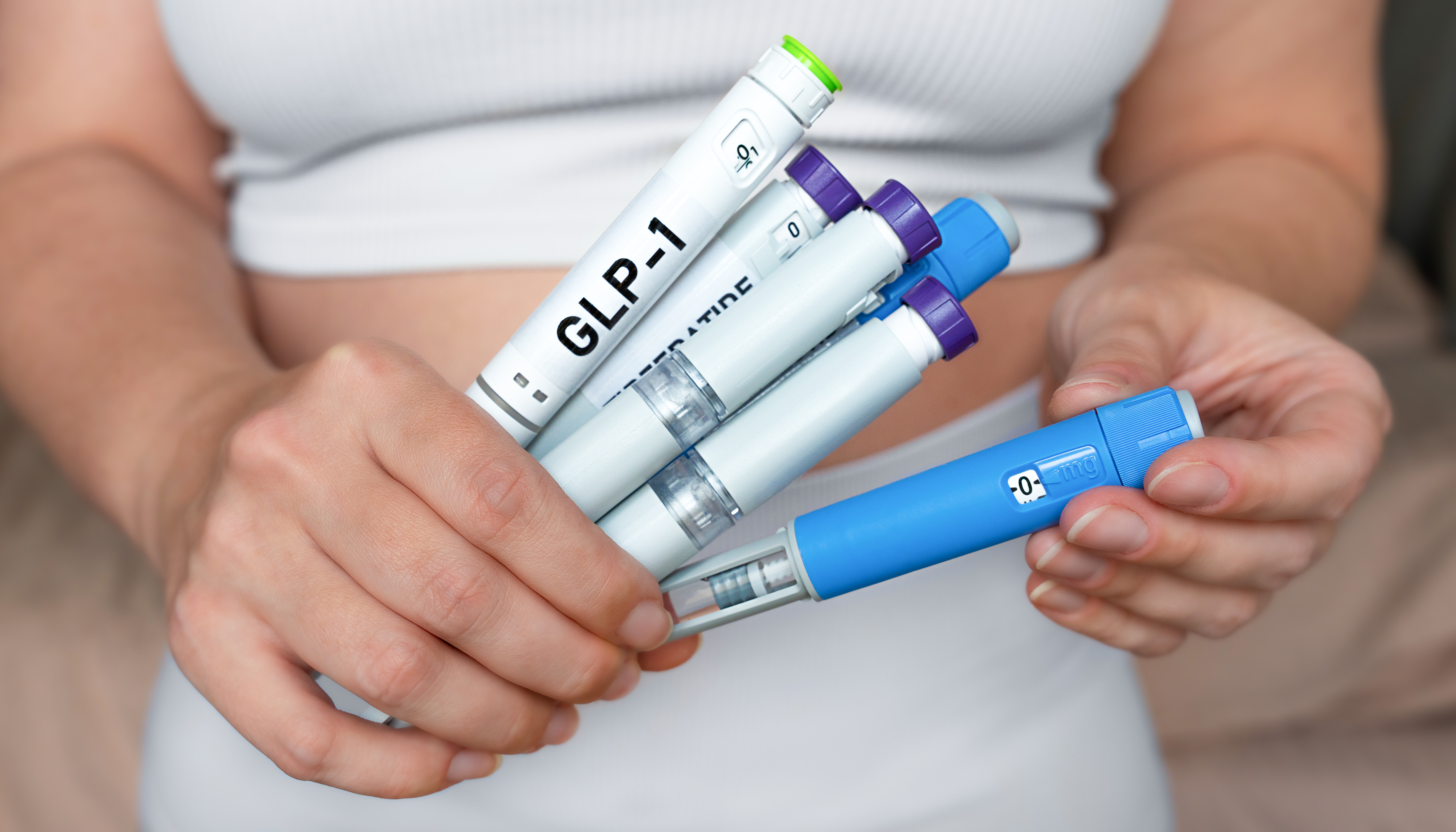 Woman holding multiple GLP-1 injection pens, weight loss and diabetes treatment concept.