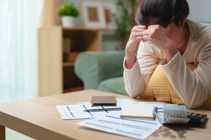 Stressed woman reviewing bills and financial documents at home, feeling worried about debt and monthly expenses. Personal finance, budgeting, financial stress, money problems and economic hardship.