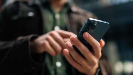 Close-up hands of unrecognizable man holding and using smartphone standing on city street, browsing internet, checking social media, using mobile application.