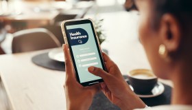 Phone screen, health insurance and hands of woman for digital application, app and check in. Claims status, membership benefits and medical cover with person for login and online review in cafe