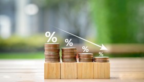 Low interest rates. Percentage sign on different high of coins stack and arrow going down.