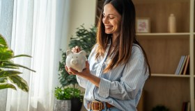 Woman smiling while putting money into piggy bank