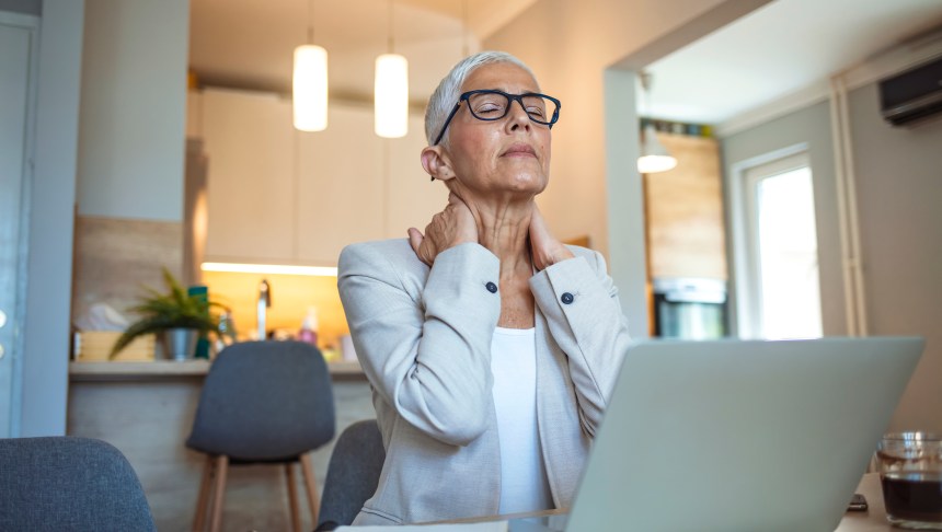 Cropped shot of a mature businesswoman looking stressed out while working in her office at home. Mature businesswoman having neck pain. Stressed mature woman massaging her neck.